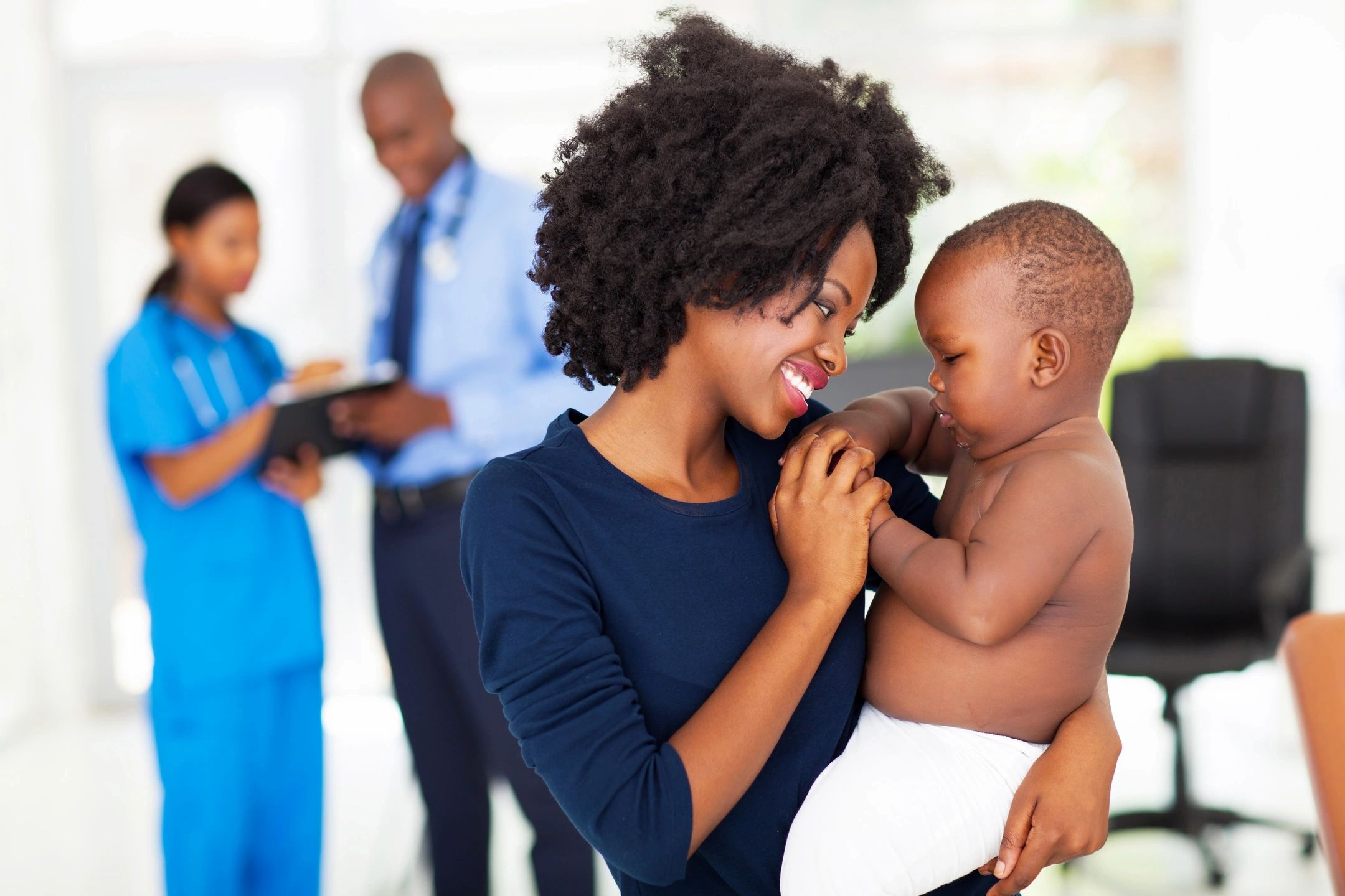A mother lovingly holds her baby while medical staff work in the background.