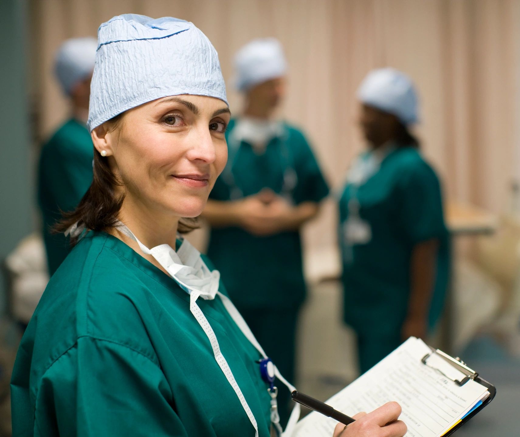 A confident female surgeon in green scrubs holding a clipboard.